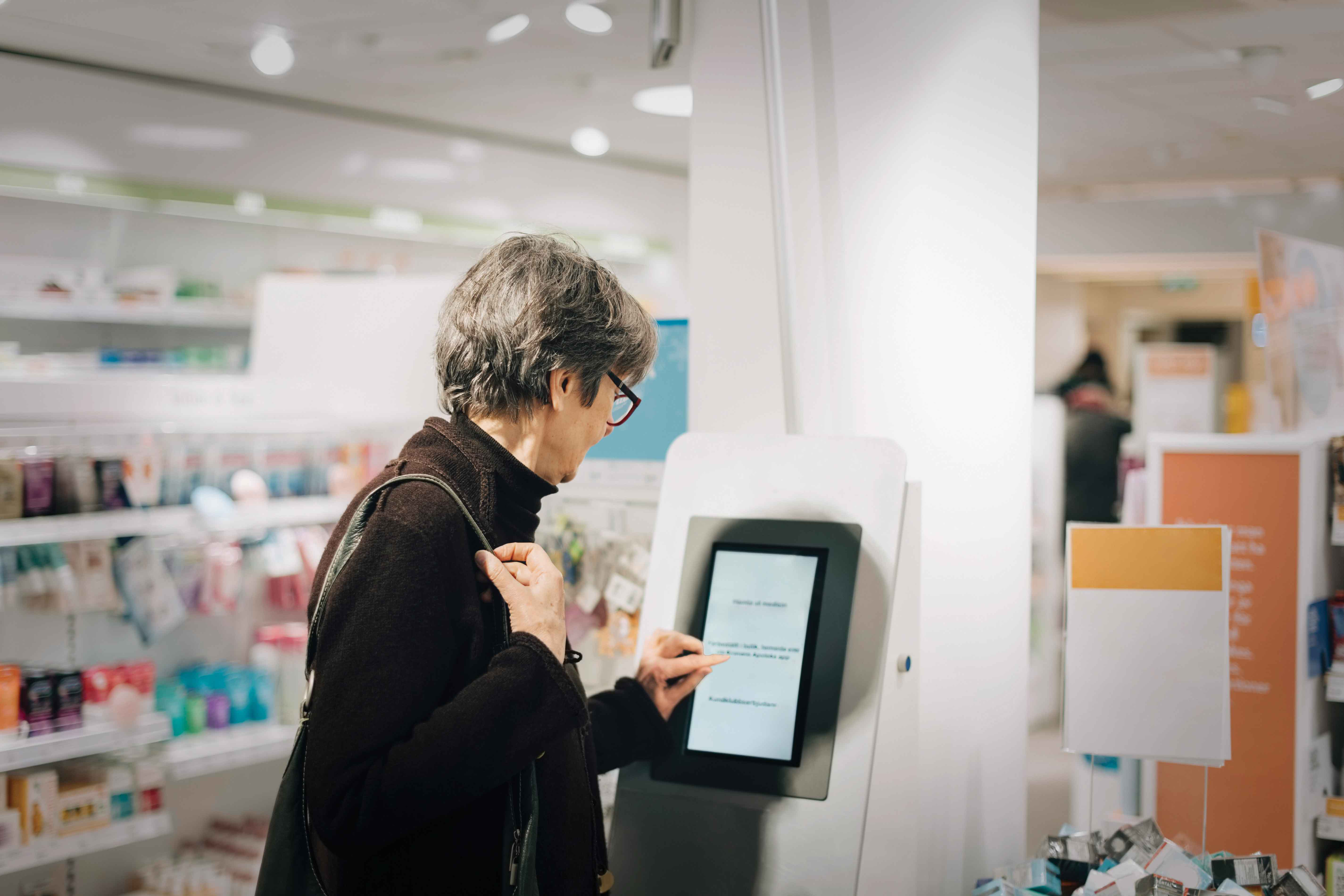 Picture of an older woman in a store shopping on a kiosk